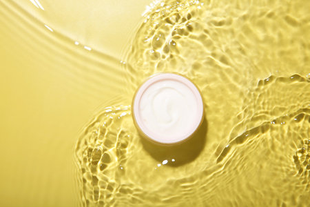 Jar with cream in water on yellow background, top view. Cosmetic productの写真素材