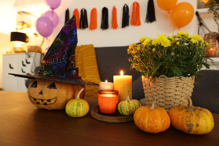 Burning candles, flowers and pumpkins on wooden table indoors. Halloween celebration