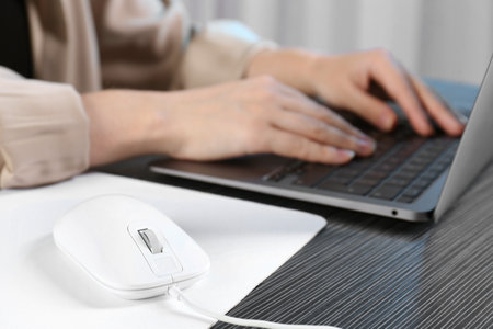 Woman working with laptop at black wooden table, focus on computer mouse