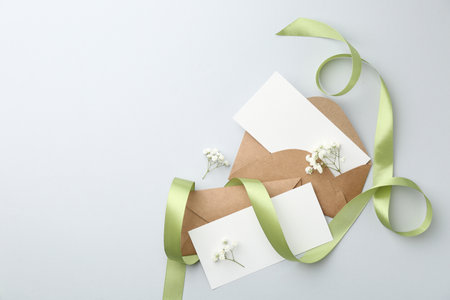 Blank cards, envelopes, flowers and ribbon on light gray table, flat lay. Space for textの写真素材
