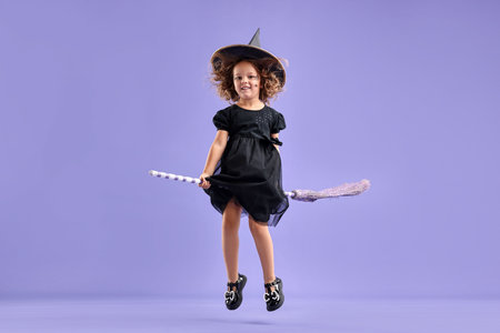 Funny girl with broom dressed like witch for Halloween celebration on violet backgroundの写真素材