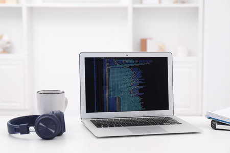 Programmer's workplace. Modern laptop with unfinished code, headphones and other supplies on white...