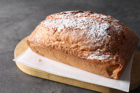 Tasty sponge cake with powdered sugar on gray table, closeup