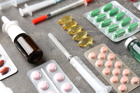 Pharmacist. Different pills, syringes and bottle of medical drops on gray table, closeup