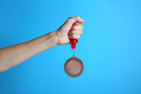 Woman with bronze medal on light blue background, closeup