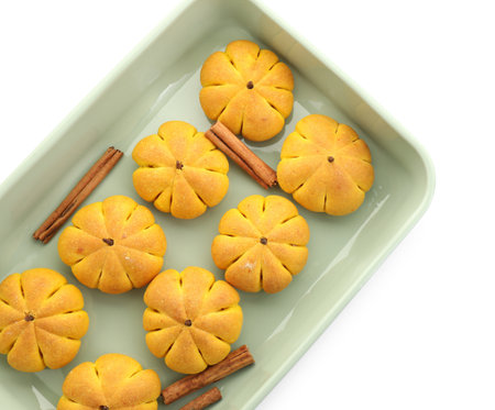 Baking tray with tasty pumpkin shaped buns and cinnamon sticks isolated on white, top view