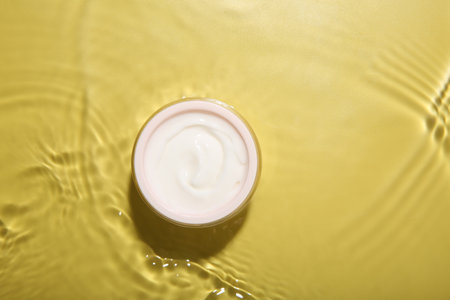 Cosmetic product. Jar with cream in water on yellow background, top view. Space for textの写真素材