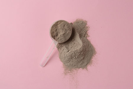 Protein powder and scoop on pink background, top view