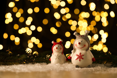 Cute decorative snowmen on artificial snow against blurred lights. Space for textの写真素材