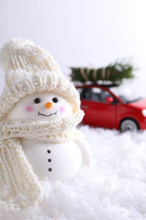 Cute decorative snowman and toy car with fir tree branches on artificial snow against light background, selective focusの写真素材