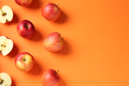 Whole and cut fresh red apples on orange background, flat lay. Space for text