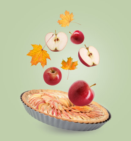 Autumn cake, apples and orange leaves in air on light green backgroundの写真素材
