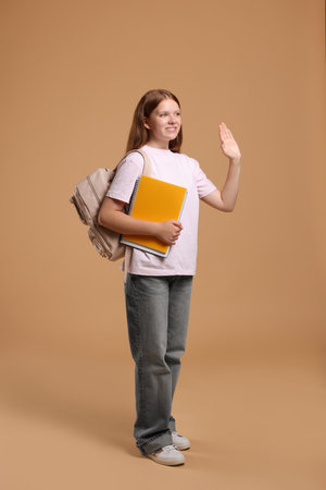 Teenage girl with backpack and books on beige backgroundの写真素材