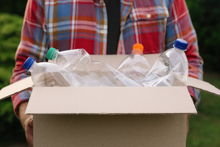 Recycling. Man holding cardboard box with plastic bottles outdoors, closeup