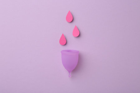 Menstrual cup with drops on violet background, top viewの写真素材