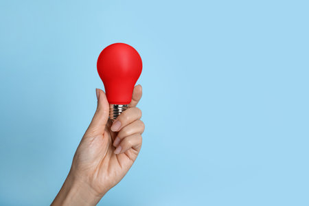 Woman holding red bulb on light blue background, closeup. Space for textの写真素材