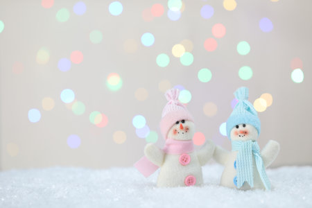 Cute snowmen against beige background with blurred lights, bokeh effectの写真素材