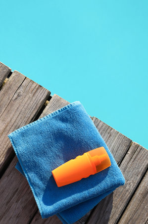 Towel and sunscreen on wooden deck near outdoor swimming pool, top viewの写真素材