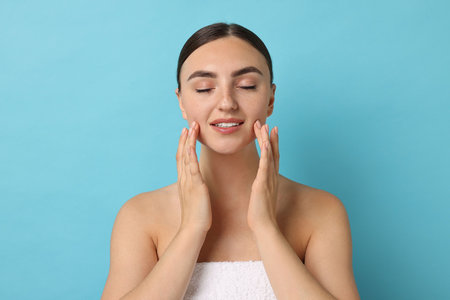 Face massage. Beautiful young woman with healthy skin on light blue backgroundの写真素材