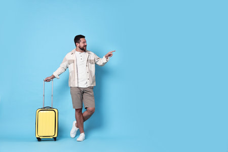 Happy man with suitcase pointing at something on light blue background, space for textの写真素材