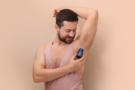 Man applying roll-on deodorant on beige backgroundの写真素材