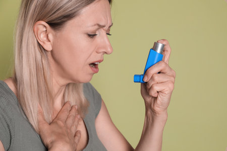 Woman using asthma inhaler on olive backgroundの写真素材