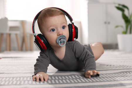 Cute little baby with pacifier and headphones on floor at homeの写真素材
