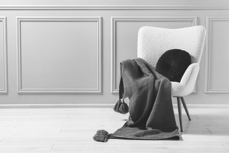 Comfortable armchair with blanket and pillow near wall indoors, black and whiteの写真素材