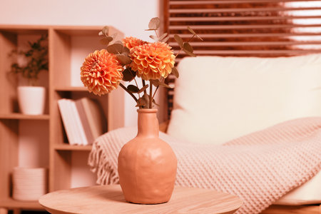 Ceramic vase with beautiful flowers on coffee table near armchair indoors, toned in orange colorの写真素材