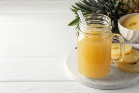 Tasty pineapple juice in mason jar and slices of fresh fruit on white wooden table, closeup. Space for textの写真素材