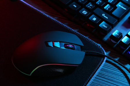 Computer mouse, mousepad and keyboard on dark wooden table in neon lights, closeupの写真素材