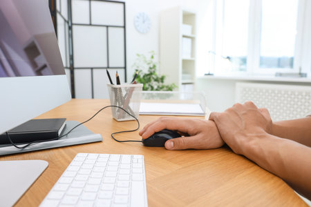 Man suffering from pain in wrist while using computer mouse at table indoors, closeup. Carpal tunnel syndromeの写真素材