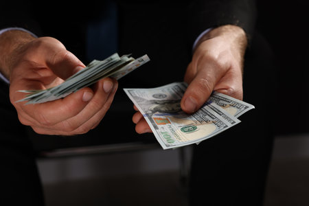 Corruption concept. Man holding dollar banknotes on black background, closeup