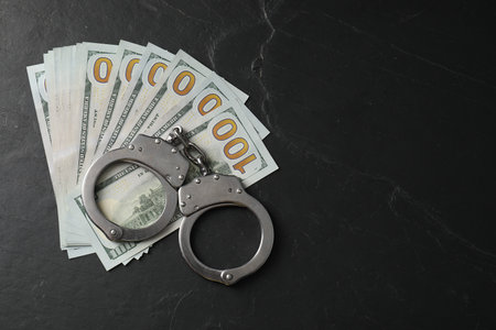 Corruption. Handcuffs and dollar banknotes on gray textured table, flat lay. Space for textの写真素材