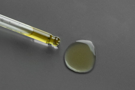 Dripping essential oil from pipette on gray background, top view