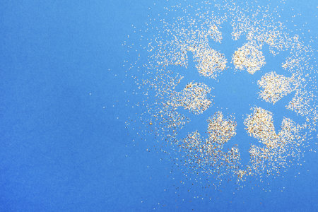 Snowflake made of golden glitter on blue background, top view. Space for textの写真素材