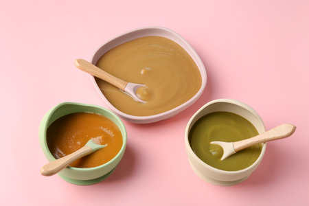 Delicious baby food and spoons in bowls on pink tableの写真素材