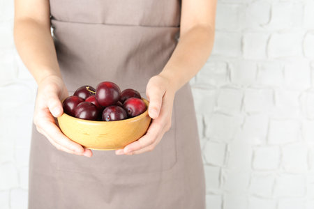 Woman holding bowl of ripe plums against white background, closeupの写真素材