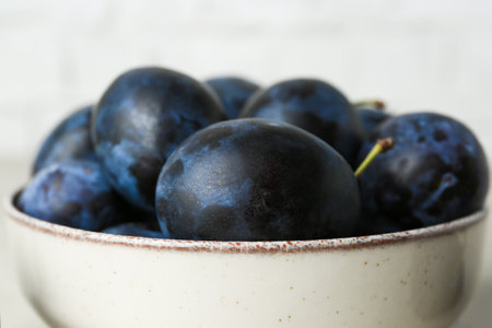 Ripe plums in bowl on table, closeupの写真素材