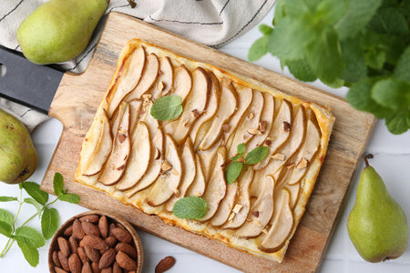 Delicious puff pastry tart with pears, almond and mint on light tiled table, flat layの写真素材