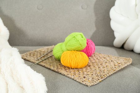 Skeins of soft yarn and knitting needles on sofa indoors