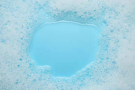 Washing laundry. White foam with bubbles on light blue background, top viewの写真素材