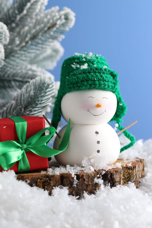 Cute decorative snowman, gift box and fir tree branches on artificial snow against light blue background, closeupの写真素材