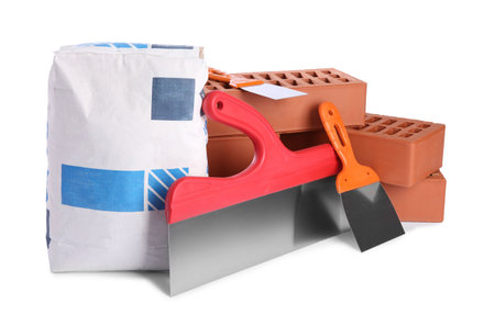 Cement powder in bag, red bricks and putty knives isolated on white. Building materials and construction toolsの写真素材