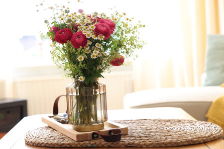 Beautiful ranunculus flowers and chamomiles in vase on table indoorsの写真素材