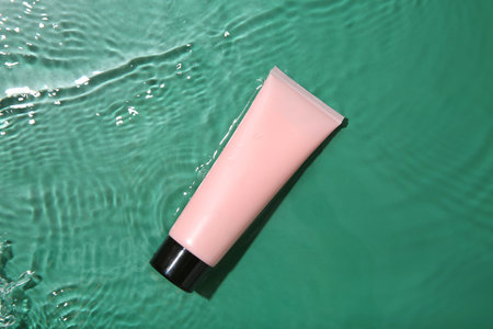 Cosmetic product. Tube with cream in water on green background, top view