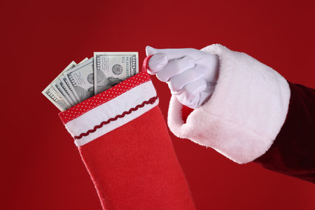 Santa holding stocking with dollar banknotes on red background, closeupの写真素材