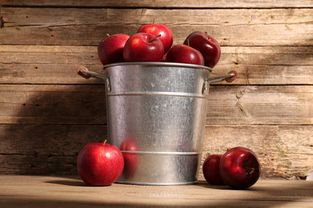 Fresh ripe red apples in bucket on wooden tableの写真素材