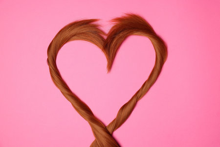 Red hair strands in the shape of heart on pink background, top viewの写真素材