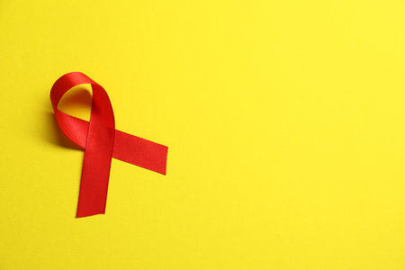 Red awareness ribbon on yellow background, top view. Space for textの写真素材